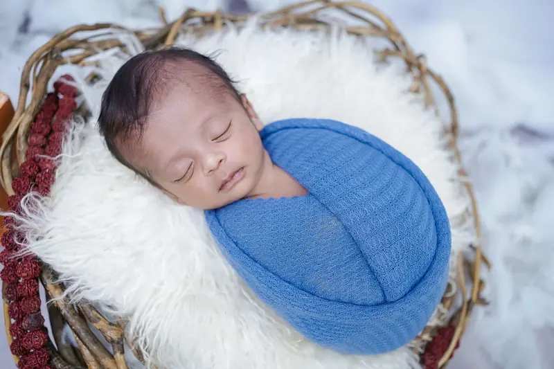 A serene newborn baby sleeping in a cozy blue swaddle, placed in a wicker basket