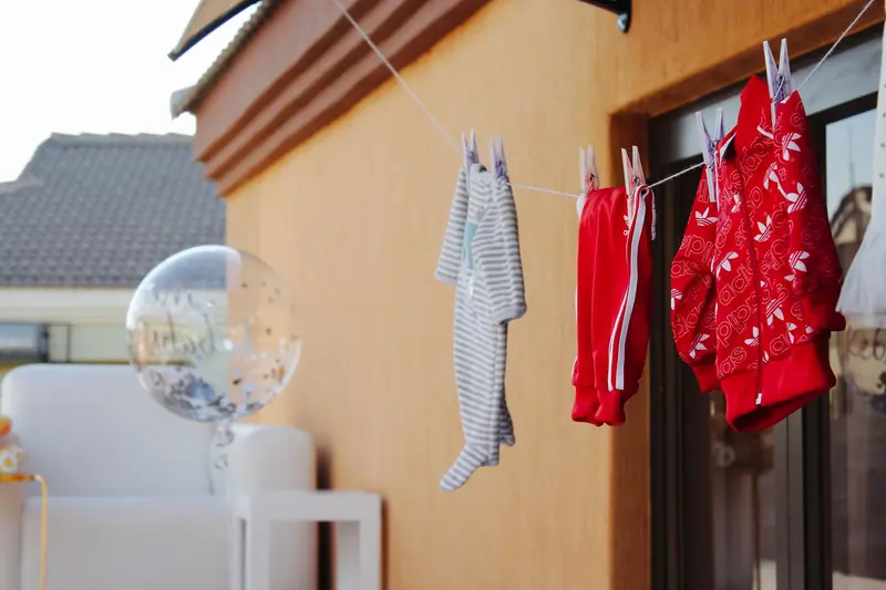 Baby clothes hanging on a clothesline next to a clear balloon against a wall