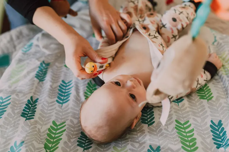 Parent using a thermometer for temperature check on a baby lying on a patterned bedspread