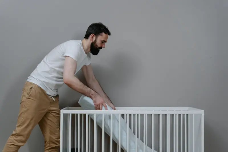 A bearded man setting up a crib in a minimalistic nursery room