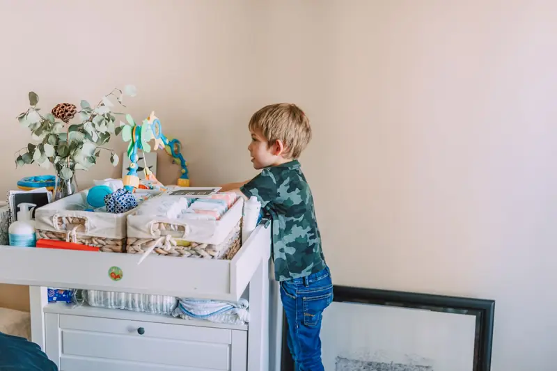 A young boy standing indoors, wearing camouflage, exploring a changing table with a playful curiosity