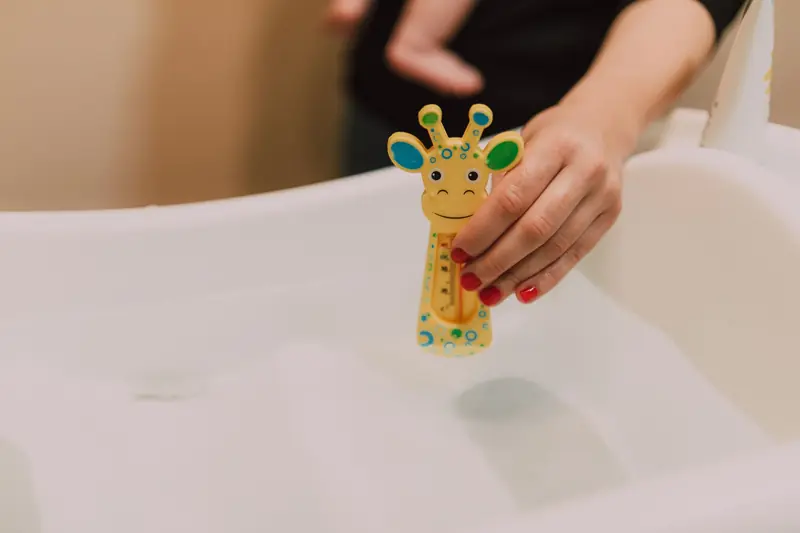 A hand holding a giraffe-shaped thermometer in a baby bath for temperature check