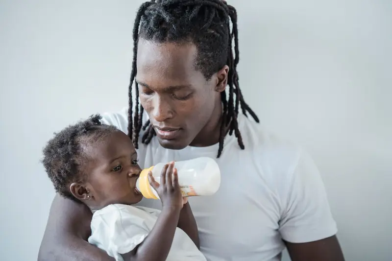 A father lovingly feeds his baby with a bottle, highlighting family bonds and warmth