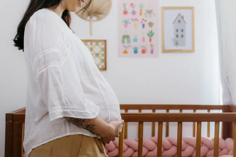 Expectant mother standing beside a wooden crib in a beautifully decorated nursery room