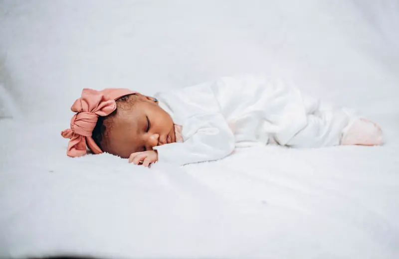 Adorable baby sleeping peacefully on white fabric, wearing a pink headband