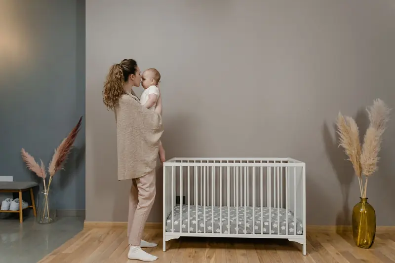 A mother gently holds her baby beside a crib in a stylish nursery