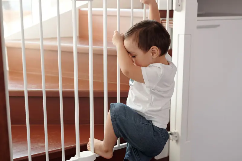 A curious toddler climbing a safety gate near stairs inside a home
