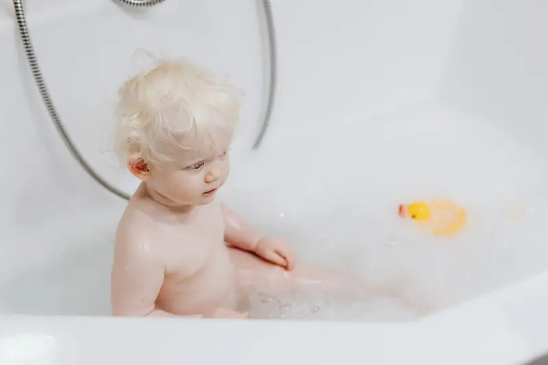 Cute blonde baby enjoying a bubble bath with a rubber duck. Perfect for hygiene and childhood concepts