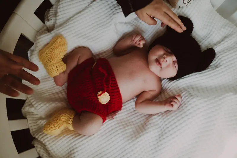A cute newborn baby wearing a handmade knit outfit in a cozy crib with loving hands nearby