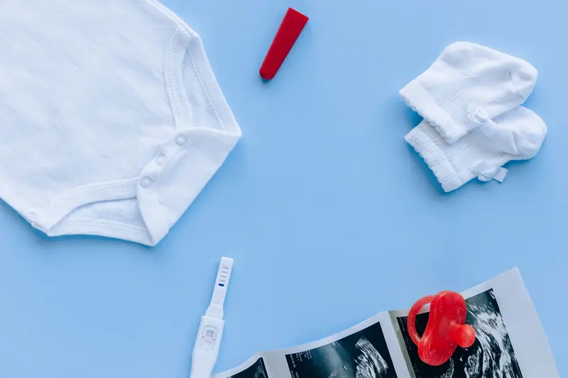 Flat lay of baby essentials and a pregnancy test on a blue background