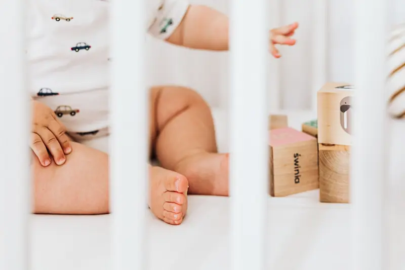A cute baby sits in a crib playing with colorful wooden blocks, showcasing a peaceful nursery environment